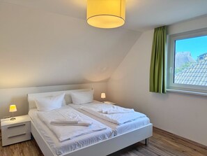 Ett sovrum med en säng, sängbord, en lampa, ett fönster med gardiner och utsikt över omgivningen.