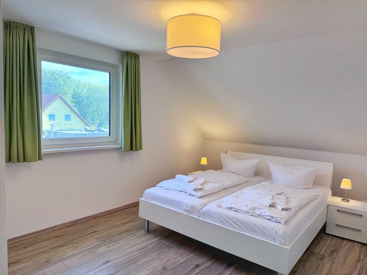 A bedroom with a bed, two bedside tables, a window with curtains, and a ceiling light fixture.