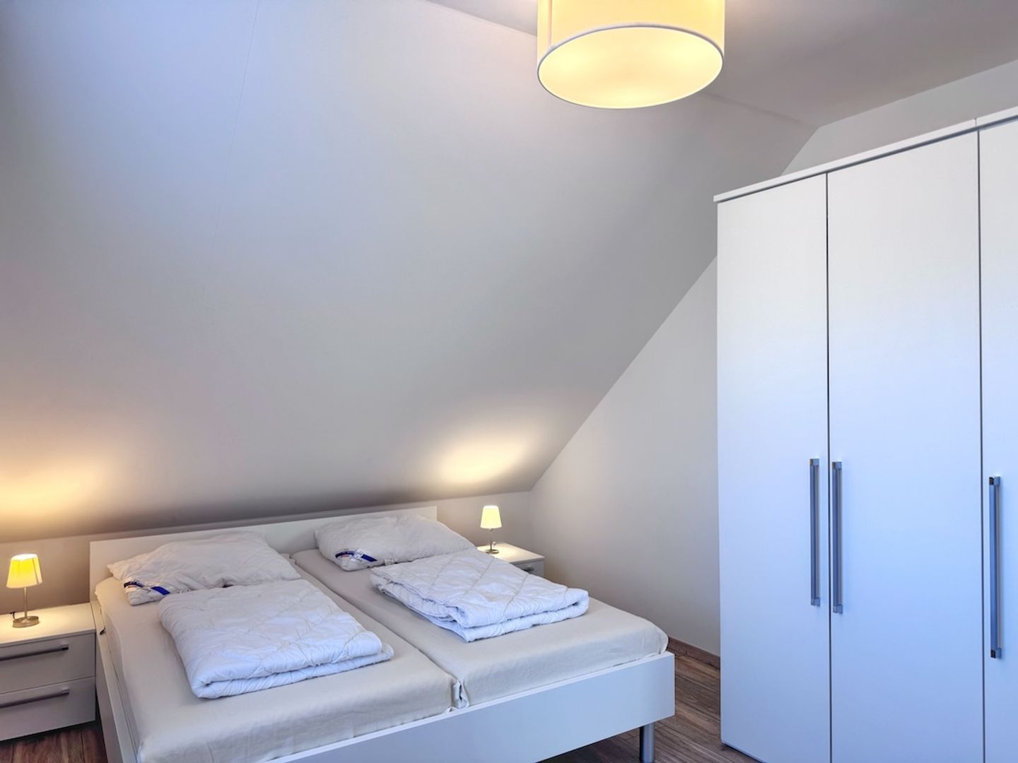 Une chambre à coucher comprenant un lit, des tables de chevet, une armoire et un luminaire au plafond.