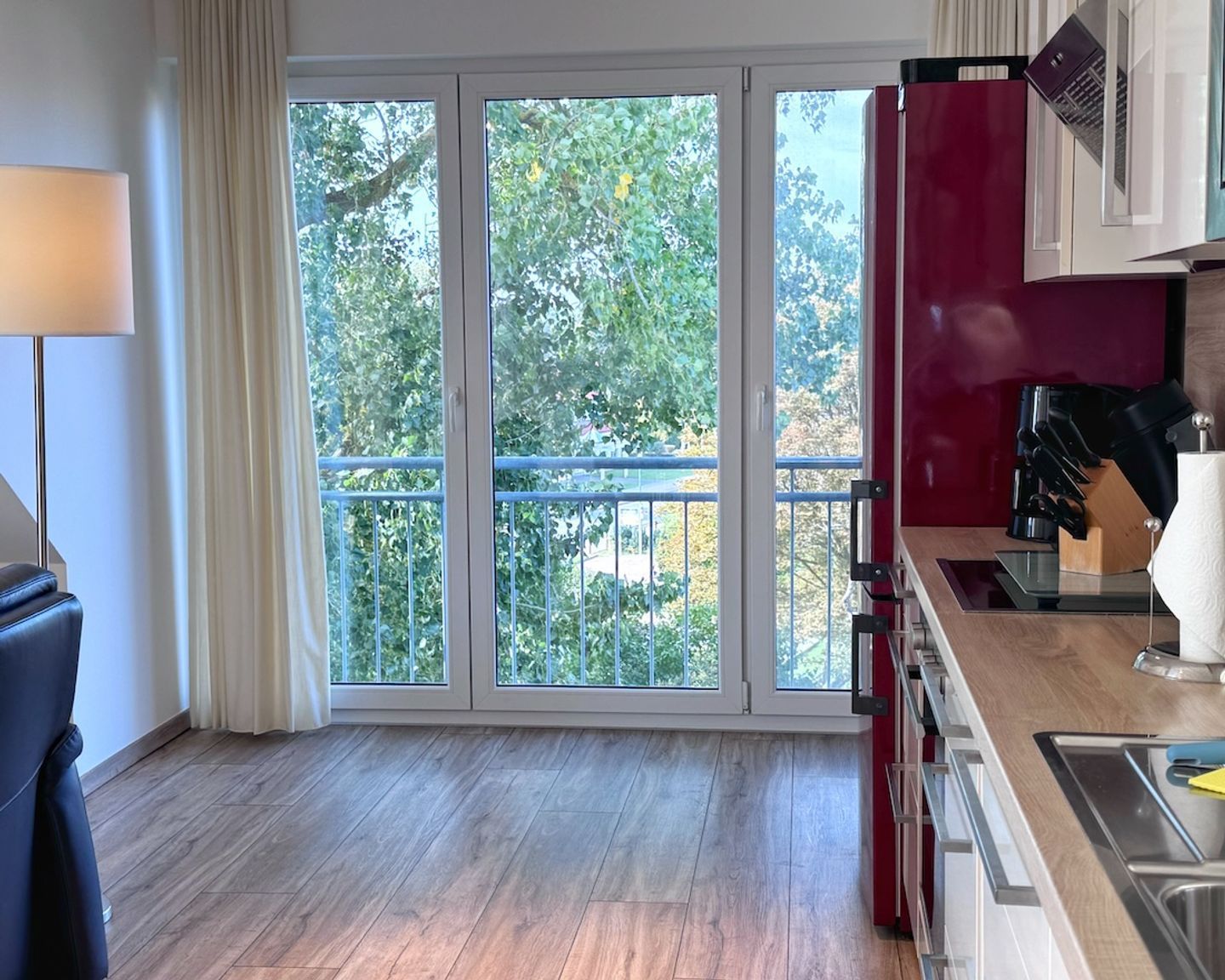 Une cuisine moderne dotée d’une grande porte-fenêtre coulissante donnant sur un balcon, d’un meuble rouge et d’une machine à café.