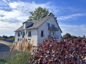 A two-story residential building with a balcony on the upper floor, surrounded by vegetation. - Three-Bedroom Vacation Apartment Near the Beach - Mein Glowe - 1st Floor, Right (Glowe)