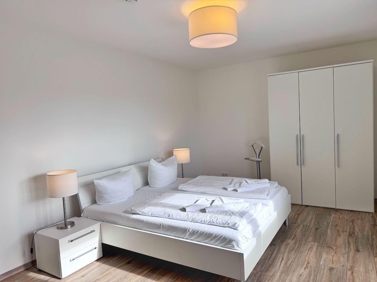 A bedroom with a bed, bedside tables, a wardrobe, and a ceiling light fixture.