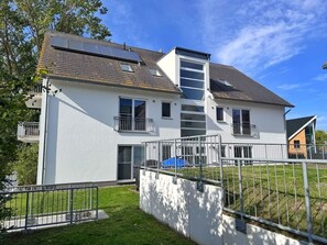 Ein zweistöckiges Wohnhaus mit weißer Fassade, einem sichtbaren Balkon und einer kleinen angebauten Garage.