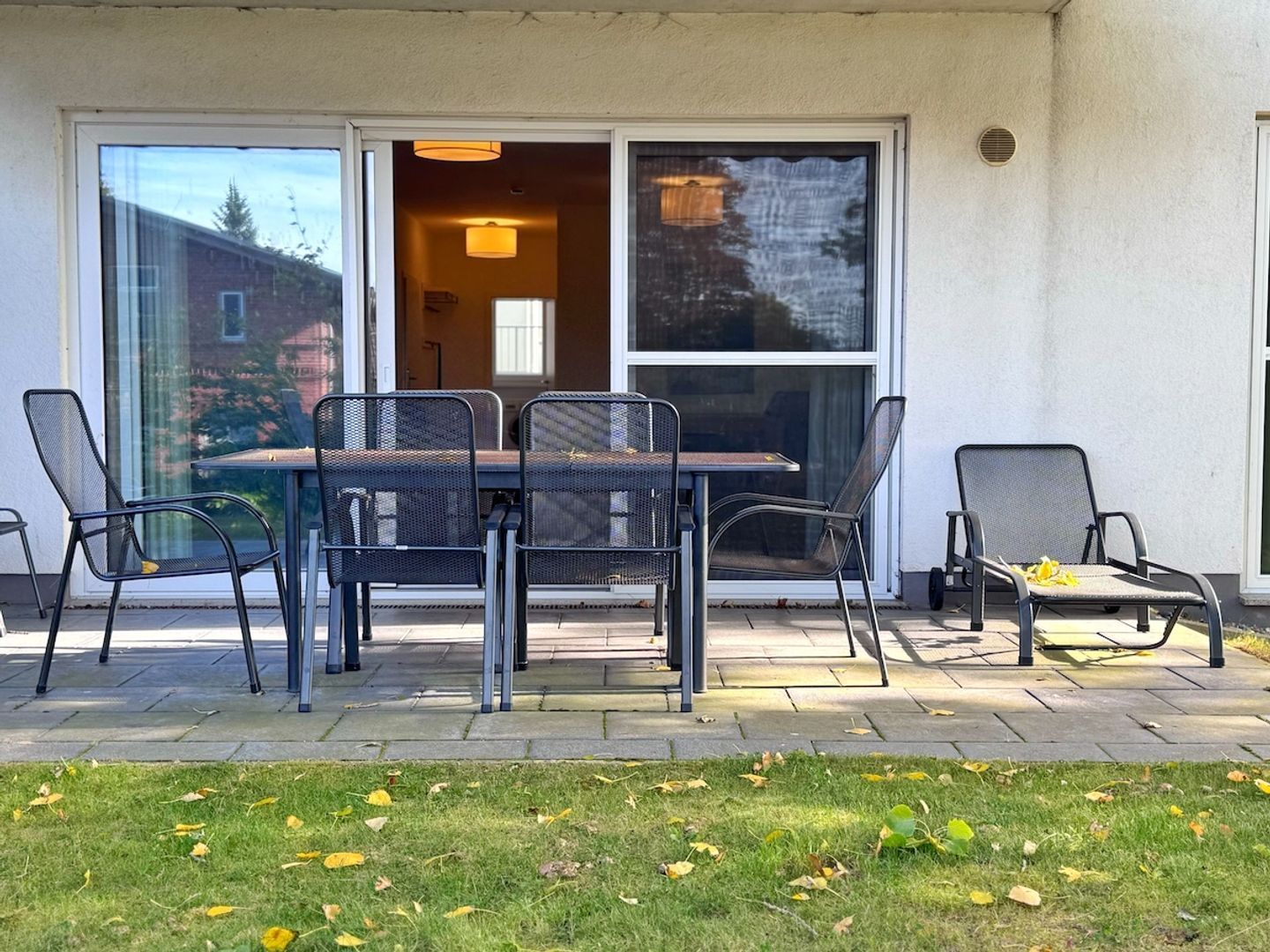 An outdoor patio with a table and chairs, a sliding glass door, and a view of a building in the background.