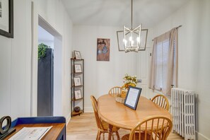 Un comedor con mesa y sillas de madera, una lámpara de araña, un radiador y un estante con marcos.