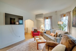 Una sala de estar con un sofá, un sillón, una mesa de centro y un televisor montado en la pared.