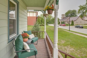 A porch with two green cushioned chairs, a potted plant, and a hanging flower basket. - Walk to Downtown Plymouth Retreat w/ Fire Pit (Plymouth)