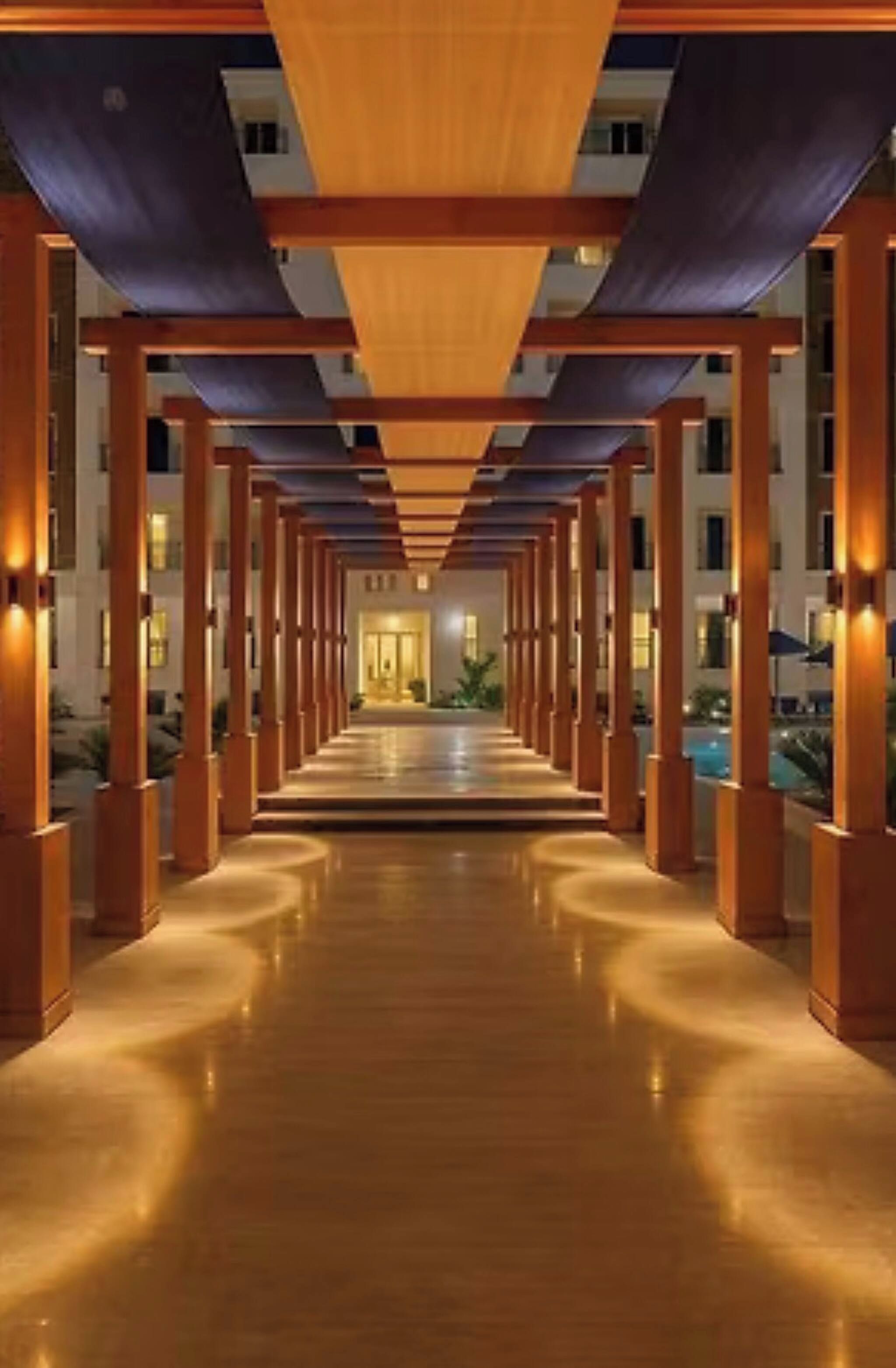 A corridor with wooden columns and a reflective floor leading to a building entrance.