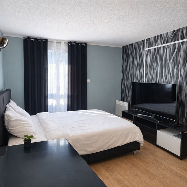 A modern hotel room with a bed, a flat-screen TV, a bedside table, and a small plant. - Comfortable & Stylish Property in a Great Location (Corrèze)
