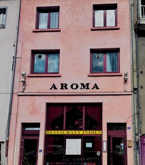 Un edificio con el nombre 'AROMA' en la fachada, con varios ventanales y un letrero que indica que es un restaurante.