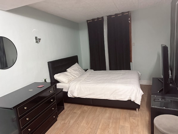 A bedroom with a bed, a dresser, a television, and a mirror.