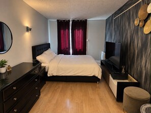 A bedroom with a bed, a dresser, a TV, and a wall-mounted shelf.