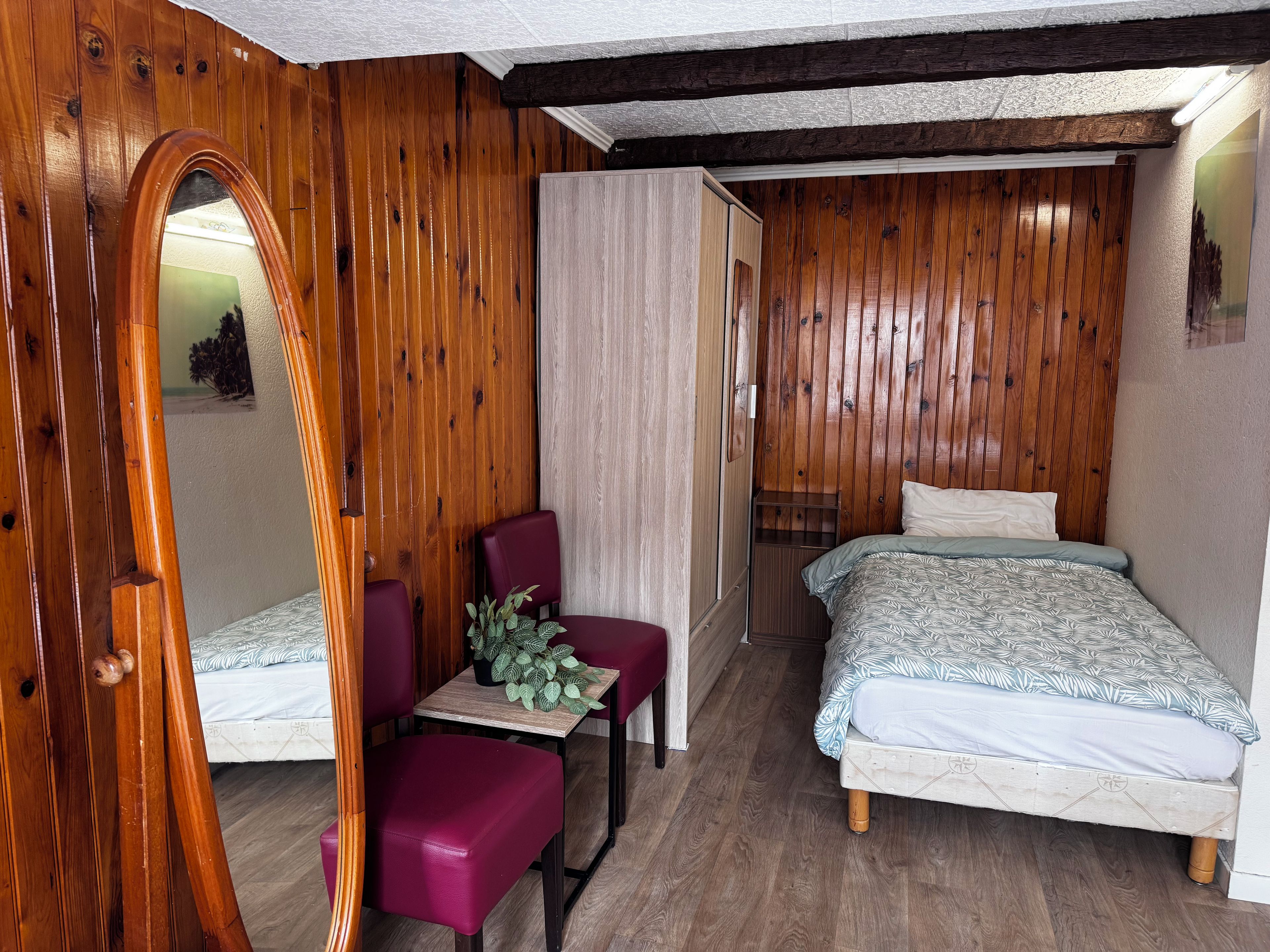 Una habitación con una cama, una silla, una mesita y un espejo.