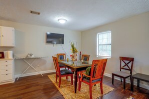 A dining area with a glass table, wooden chairs, a small rug, a flat-screen TV mounted on the wall, and a window with blinds. - 7 Mi to Mall of Georgia: Fire Pit & Yard (Buford)