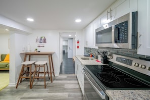 Eine moderne Küche mit Einbauofen, Mikrowelle und Edelstahlgeräten. Ein Holztisch mit Hockern und eine kleine Pflanze an der Wand sind ebenfalls vorhanden.