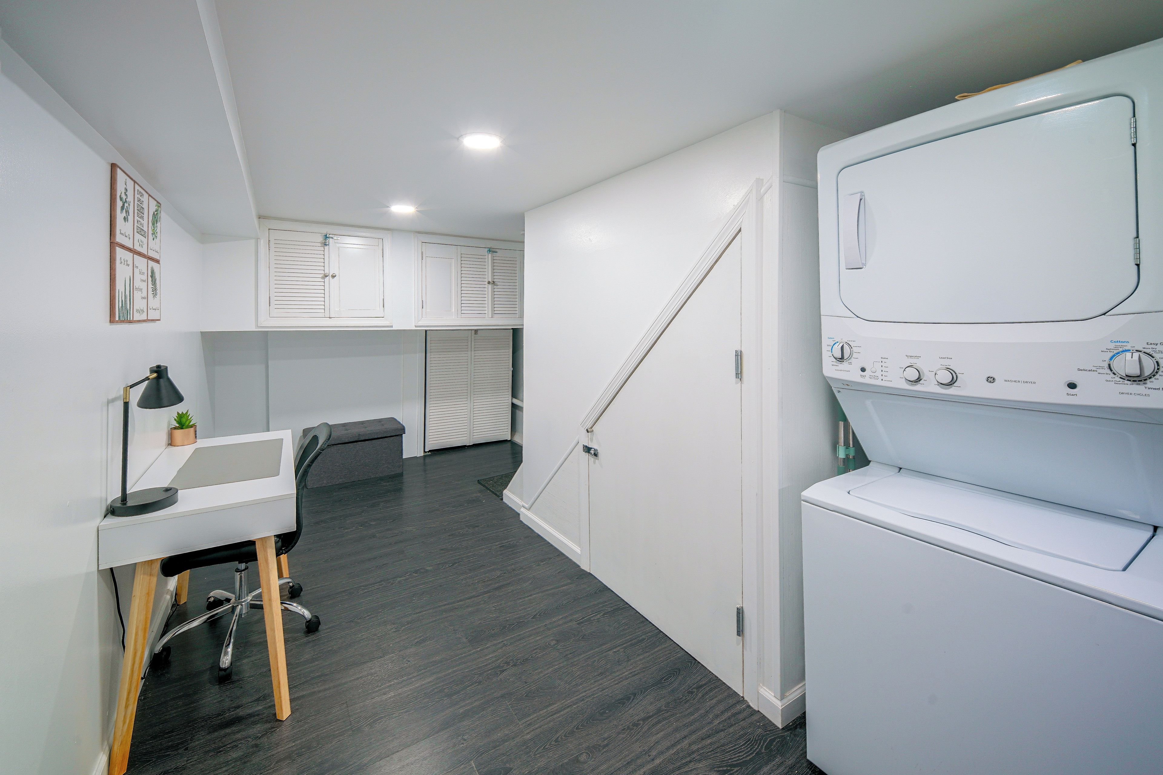 A laundry room with a washing machine, a desk with a lamp, and a small plant.