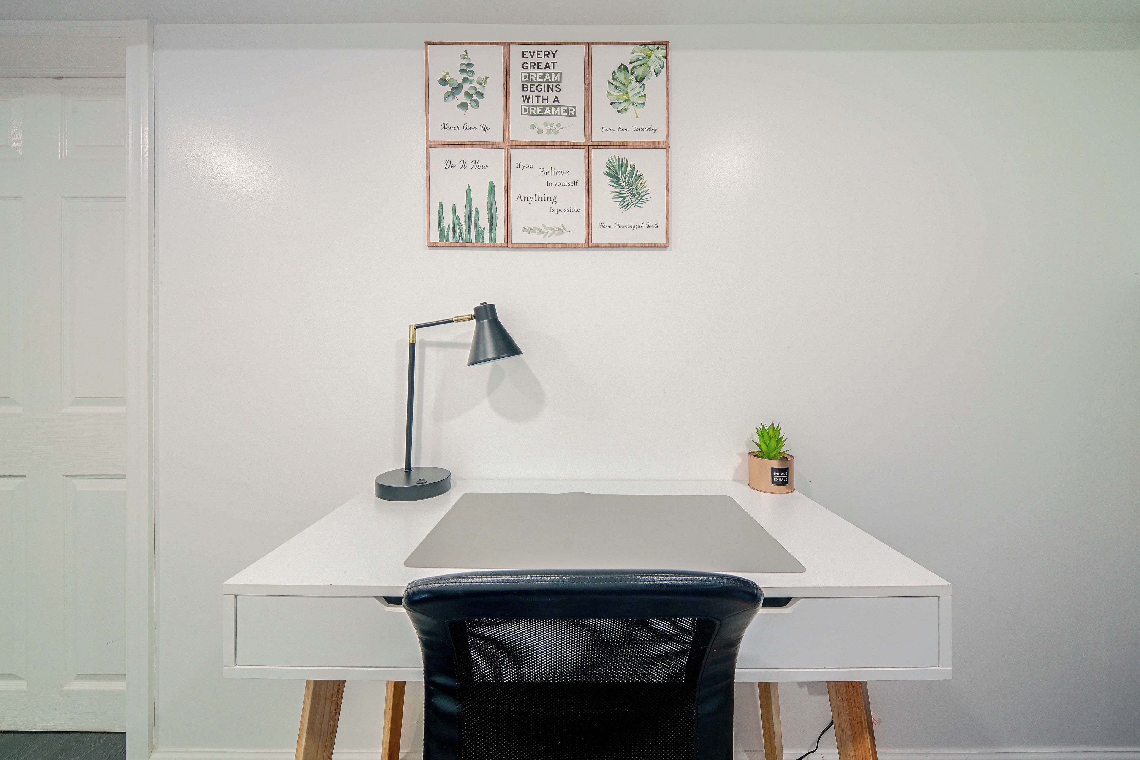 A white desk with a black mesh chair, a black desk lamp, and a small potted plant.
