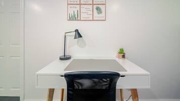 A white desk with a black mesh chair, a black desk lamp, and a small potted plant.