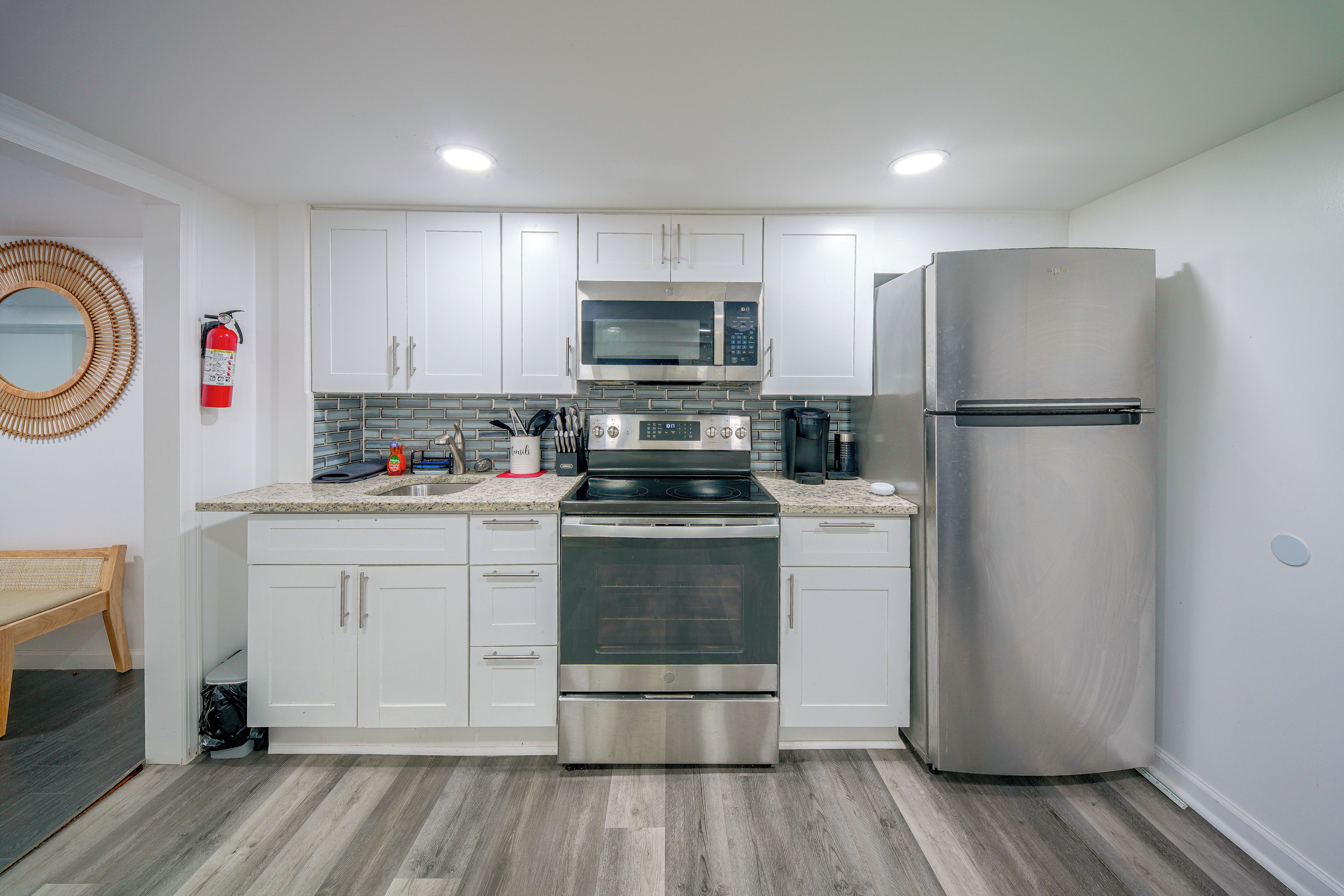 A modern kitchen with white cabinets, stainless steel appliances, and a wooden floor.