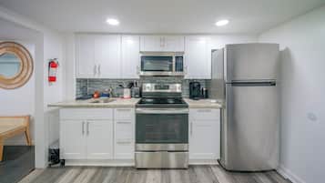 A modern kitchen with white cabinets, stainless steel appliances, and a wooden floor.