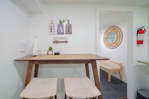 Ein Essbereich mit einem Holztisch, zwei gepolsterten Stühlen, einem an der Wand befestigten Spiegel und einem Feuerlöscher.