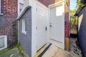 Een witte deur met raam, een bakstenen muur en een metalen hek.