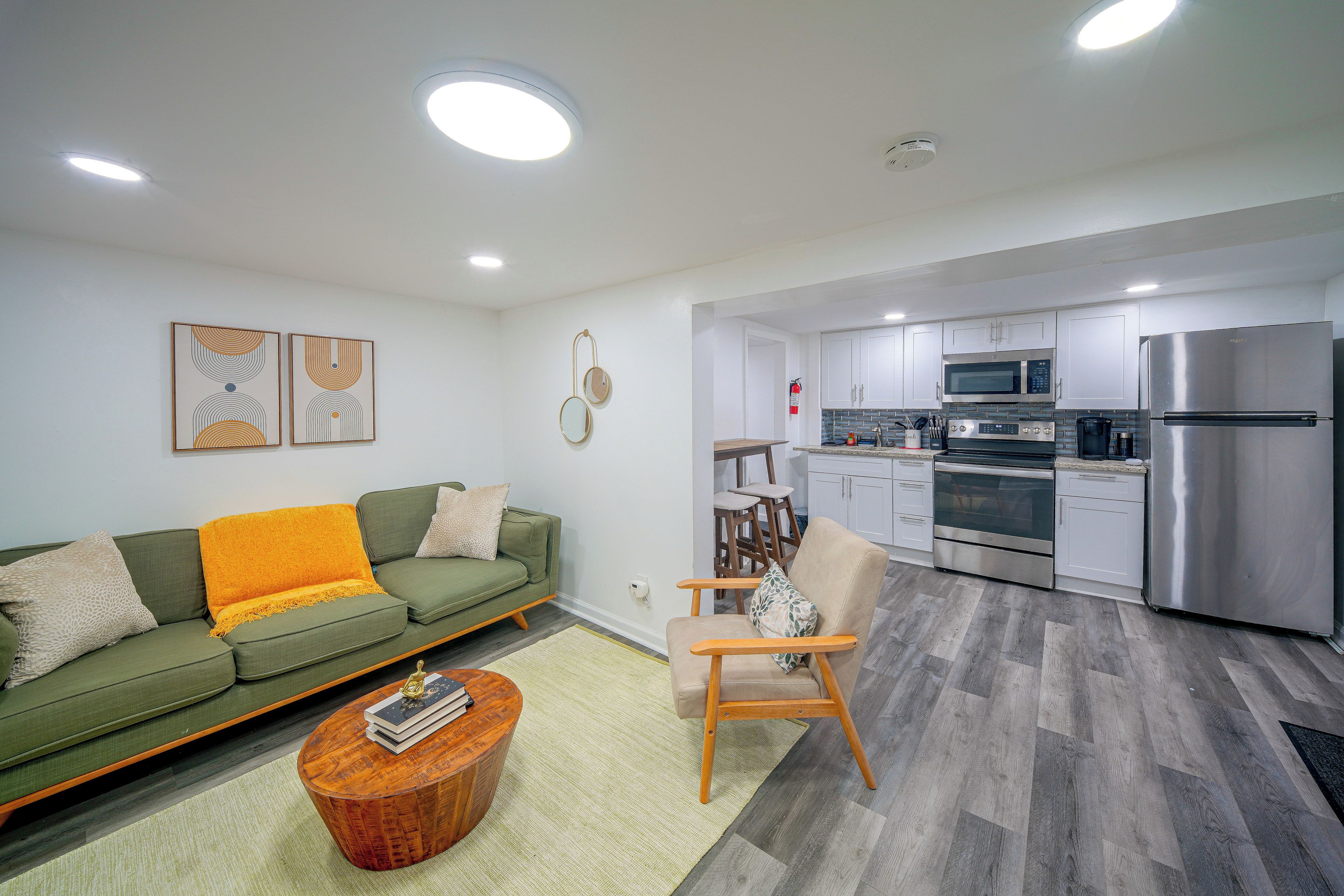 A modern living room with a green sofa, a wooden coffee table, and a kitchen area with stainless steel appliances.