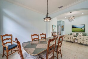 A dining area with a checkered table and wooden chairs, a chandelier, and a sofa in the background. - Tee Times + Poolside Vibes! Extended Naples Escape (Naples)