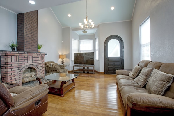 A spacious living room with a brick fireplace, leather sofas, a glass coffee table, and a television. - 4 Mi to Bourbon St & Superdome! Spacious Home (New Orleans)