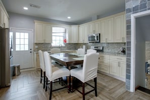 A modern kitchen with white cabinetry, a marble countertop, a stainless steel refrigerator, and a dining area with a wooden table and chairs. - 4 Mi to Bourbon St & Superdome! Spacious Home (New Orleans)