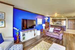 A modern living room with a flat-screen TV, a leather sofa, and a dining area with wooden cabinets and a kitchen. - Grand Lake Golf Course Getaway: Stunning Views! (Afton)