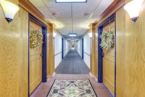 A hotel hallway with wooden doors, a patterned carpet, and wall-mounted light fixtures. - Grand Lake Golf Course Getaway: Stunning Views! (Afton)
