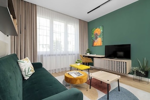 Ein modernes Wohnzimmer mit einem grünen Sofa, einem gelben Beistelltisch, einem Flachbildfernseher und einem Bild an der Wand.