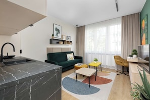 Ein moderner Wohnraum mit Küchenzeile, einem grünen Sofa, einem gelben Tisch und einem Fernseher.