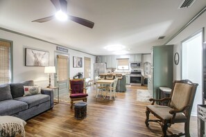 A spacious living area with a sofa, chairs, a dining table, and a kitchen in the background.