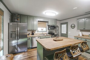 A kitchen with a central island, stainless steel appliances, and wooden chairs.