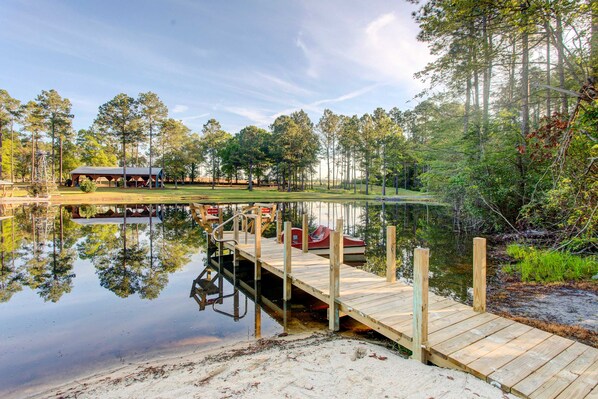 A wooden dock extending into a calm lake, surrounded by trees and a covered area with a boat docked nearby.
