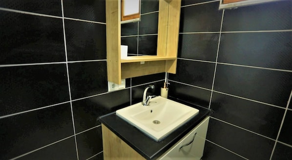 A bathroom with a white sink, black tiles, and a wooden cabinet above the sink.
