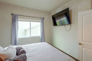 A bedroom with a bed, a window with curtains, a flat-screen TV mounted on the wall, and a door. - 1 Mi to Flanagan Park & Golf! Peaceful Home (Bennington)