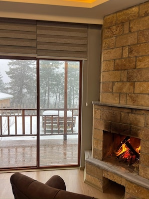 Una habitación con chimenea, una puerta corrediza de vidrio que da a un balcón nevado y un sofá marrón.