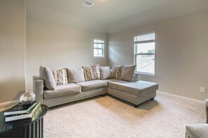 A living room with a sectional sofa, a small table with books, and a window with blinds. - Yard, Patio! Spacious Family Home By The Woodlands (Conroe)