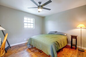 A bedroom with a bed, a ceiling fan, a window, a lamp, and a wooden floor. - 9 Mi to Six Flags! Wooded Retreat w/ Patio (San Antonio)