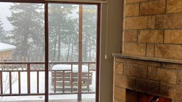 Una habitación con chimenea, una puerta corrediza de vidrio que da a un balcón nevado y un sofá marrón.