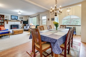 A dining area with a table set for six, surrounded by wooden chairs, a chandelier, and a fireplace in the background. - Half-Mile to Beach! Coastal Washington Hideaway (Grayland)