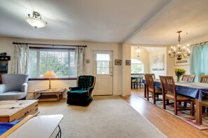 Un salon spacieux avec une grande fenêtre, un coin repas doté de meubles en bois et un lustre.