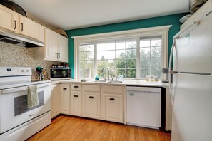 Una cocina con armarios blancos, microondas, estufa, fregadero y refrigerador.