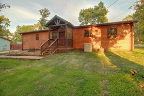 Une cabane en rondins à deux étages, dotée d’un porche à l’avant, d’un petit garage attenant et d’une pelouse bien entretenue.
