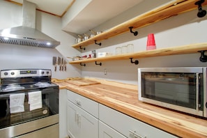 A kitchen with a stove, oven, microwave, wooden shelves, and hanging utensils. - 1/2 Mi to Marina! Modern Bull Shoals Lake Cabin (Bull Shoals)
