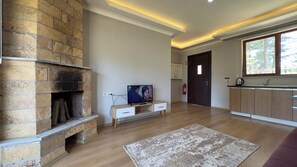 Una sala de estar moderna con chimenea de piedra, televisor de pantalla plana, piso de madera y vista al exterior a través de un ventanal.