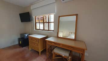 Une pièce comprenant un bureau, une chaise, un téléviseur fixé au mur et une fenêtre avec des stores.